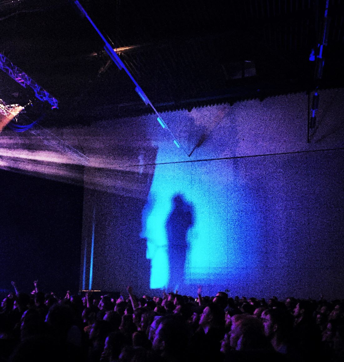Ein Schatten einer Person in blauem Licht an einer Wand, darunter die Köpfe vieler Menschen.