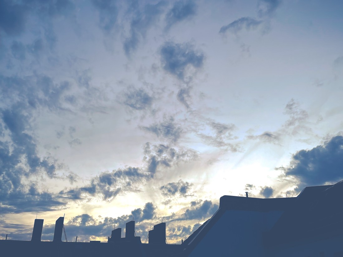 Sonnenuntergang hinter einem Haus, von dem nur Teile des Dachs und einzelne Schornsteine zu sehen sind