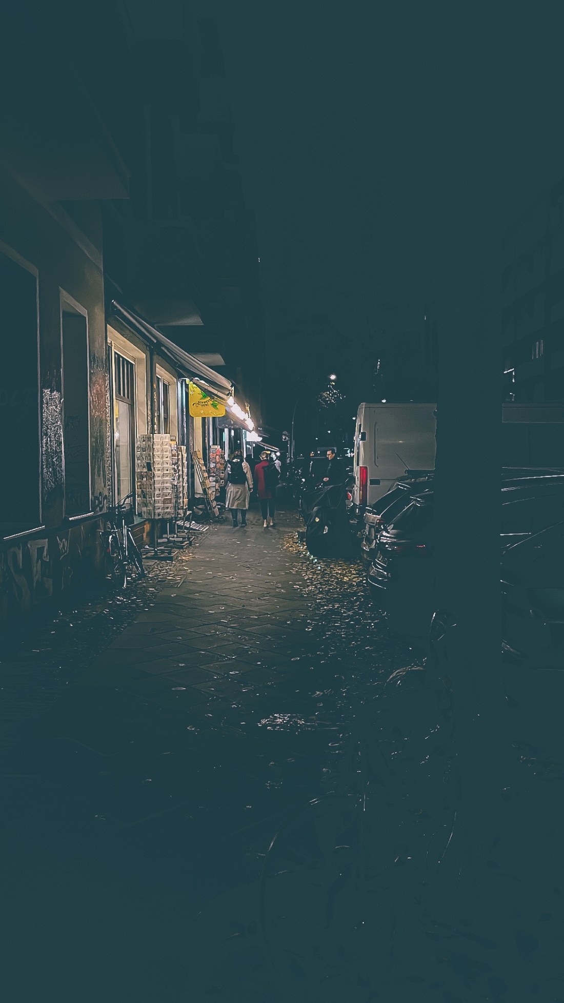 Bürgersteig im Dunkel, Schaufenster leuchten, Fußgänger verschwinden im Licht, rundherum ist alles Dunkel