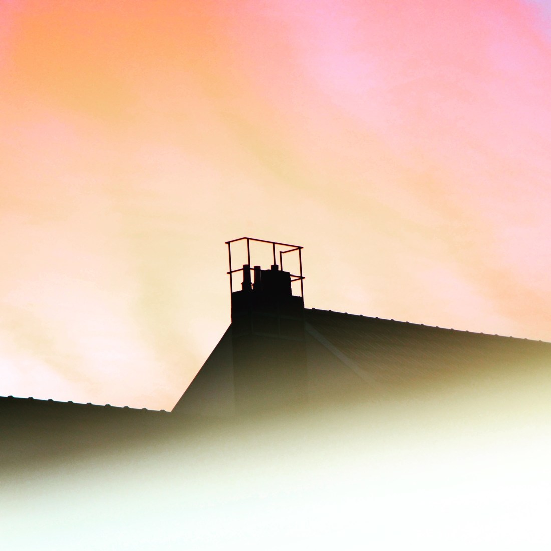 Blick auf einen Schornstein mit einem Metallgeländer rundherum. Links und rechts sind zwei Ziegeldächer zu sehen. Der Himmel erstrahlt in Gelb und Rottönen.