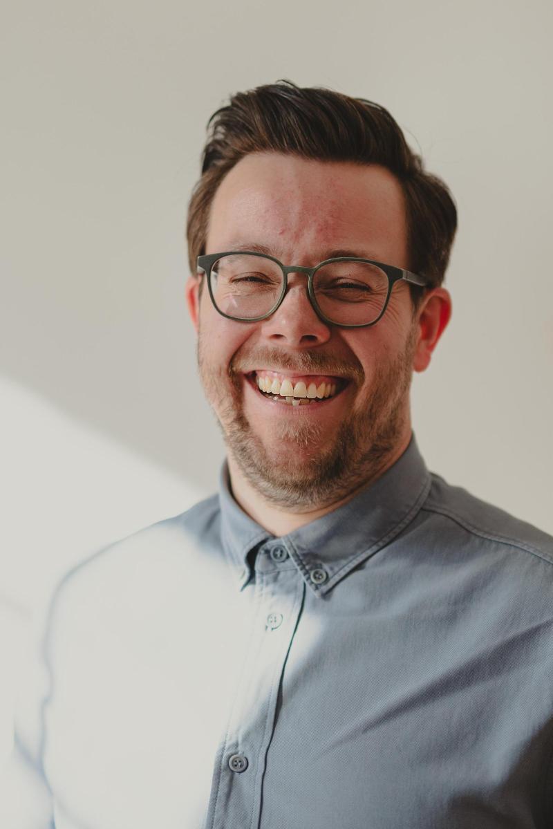 Oberkörper eines Mannes mit Brille lacht, die Sonne scheint von links auf seine Brust