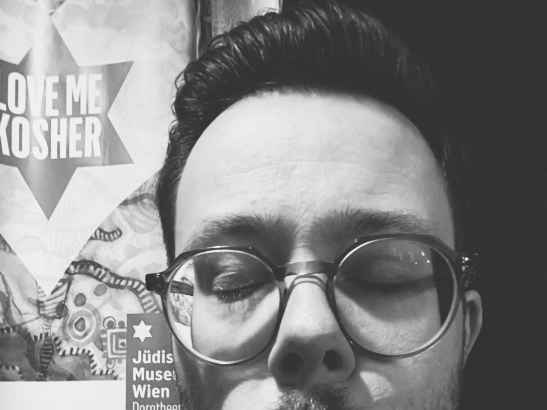 Oberer Teil eines Gesichts mit Brille, daneben ein Plakat mit der Worten „Love Me Kosher“.