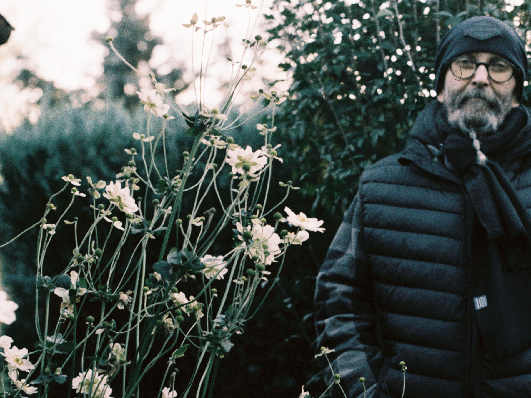 Mann mit geflochtenem Bart, Schal und Mütze, im Vordergrund Blumen